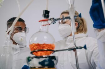 Two scientists in PPE conducting experiments with lab equipment, focusing on chemical reactions.