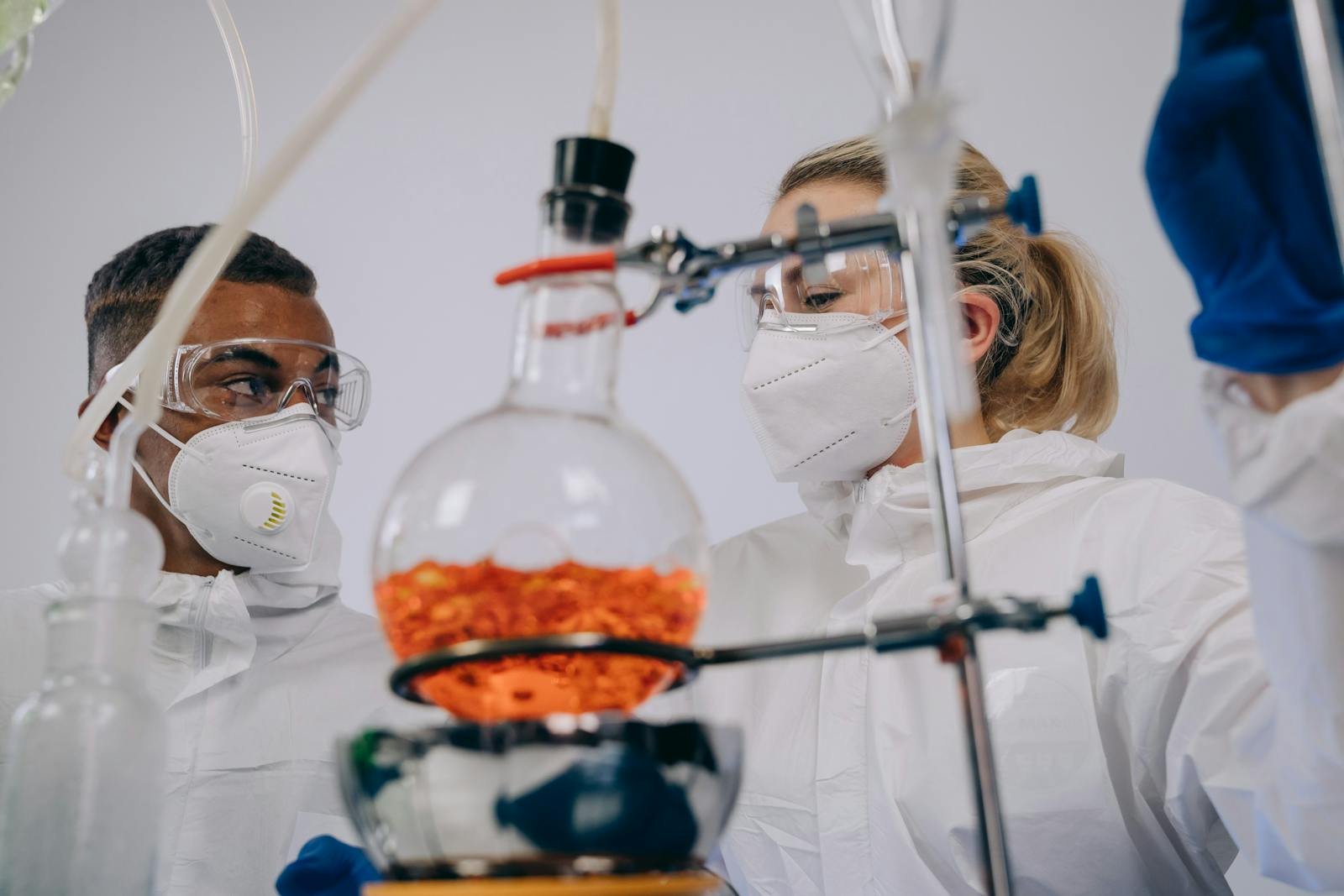 Two scientists in PPE conducting experiments with lab equipment, focusing on chemical reactions.