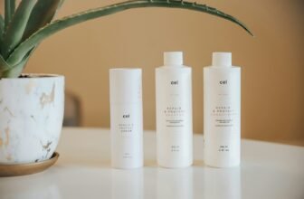 three bottles of lotion sitting on a table next to a potted plant, shampoo