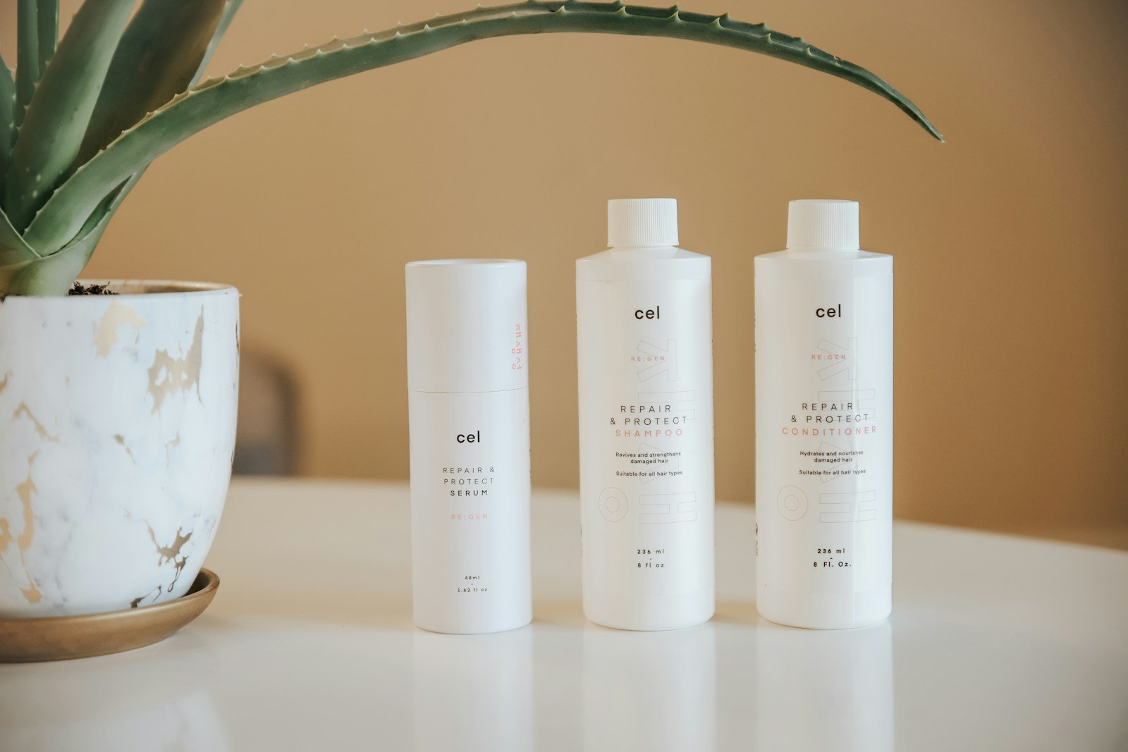 three bottles of lotion sitting on a table next to a potted plant, shampoo